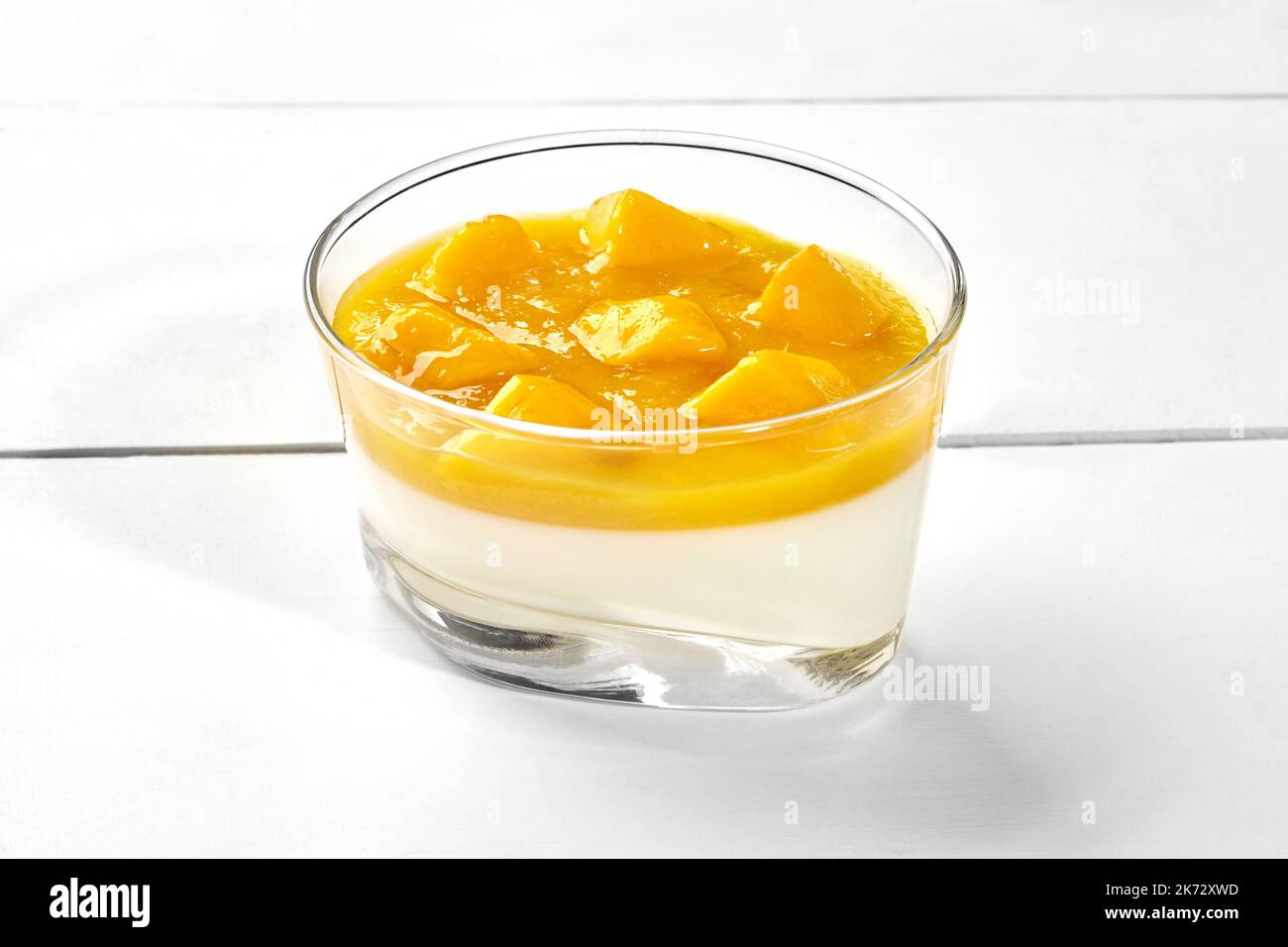 Vanilla Panna Cotta mit Mangopüree in Glas auf weißem Holzhintergrund Stockfoto