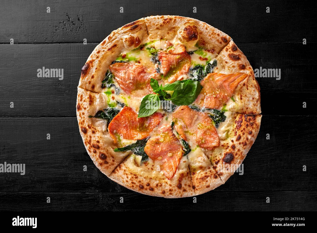 Pizza mit Frischkäse-Sauce, Lachs, Spinat, Pesto und frischem Basilikum auf schwarzer Holzoberfläche Stockfoto