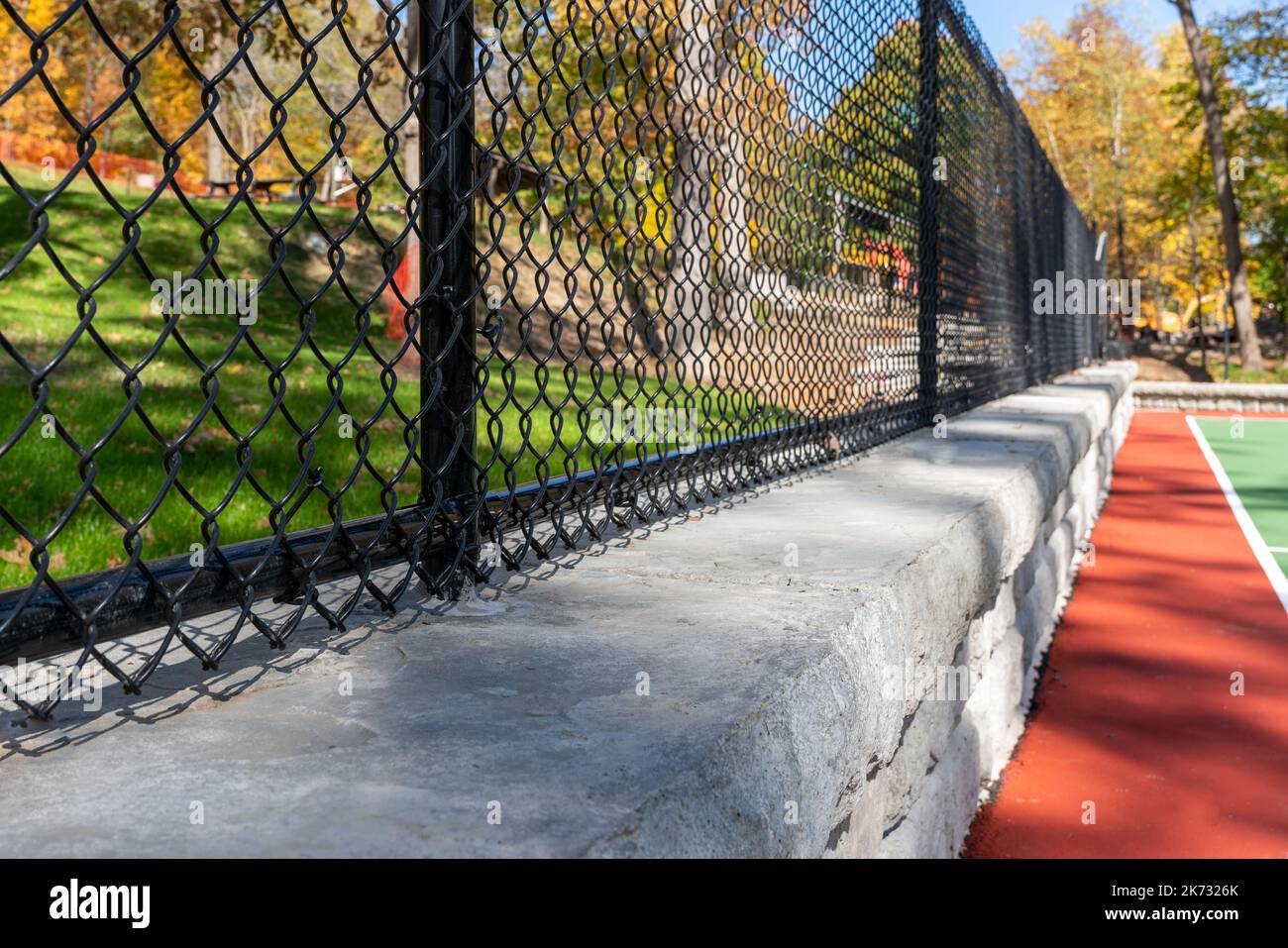 Interessanter grüner und roter Outdoor-Basketballplatz auf dem Schulhof. Das Gericht umfasst Stützmauern und einen mit schwarzem Vinyl beschichteten Kettengliederzaun. Stockfoto