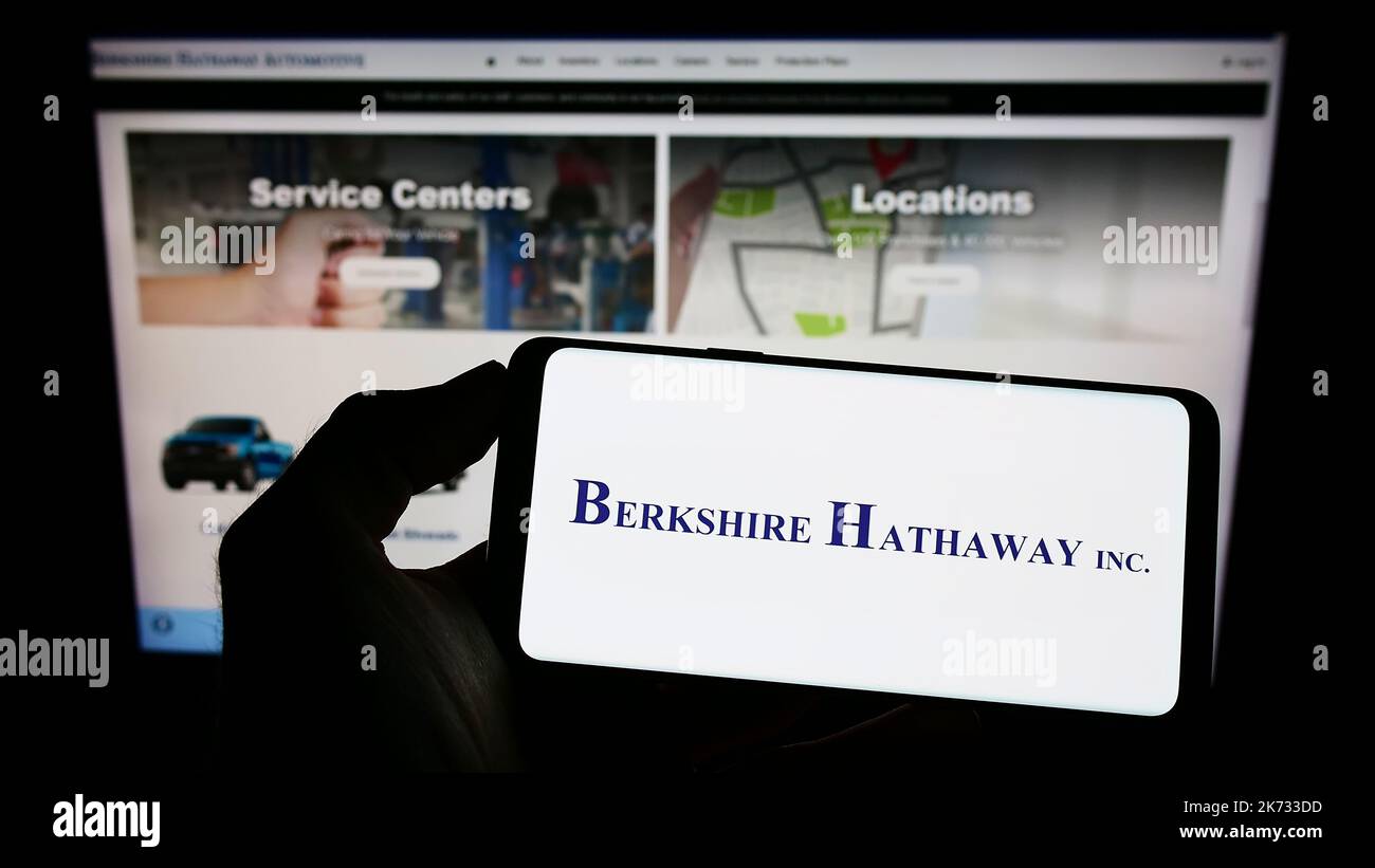 Person, die Mobiltelefon mit dem Logo der amerikanischen Holdinggesellschaft, der Firma, der Firma, auf dem Bildschirm vor der Webseite hält. Konzentrieren Sie sich auf die Telefonanzeige. Stockfoto