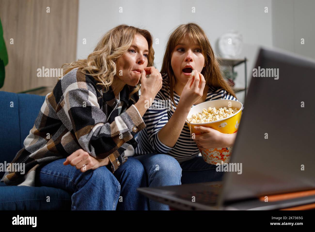 Zwei Frauen unterschiedlichen Alters mit Popcorn auf der Couch verbringen ihre Freizeit damit, Filme auf ihren Laptops zu sehen Stockfoto