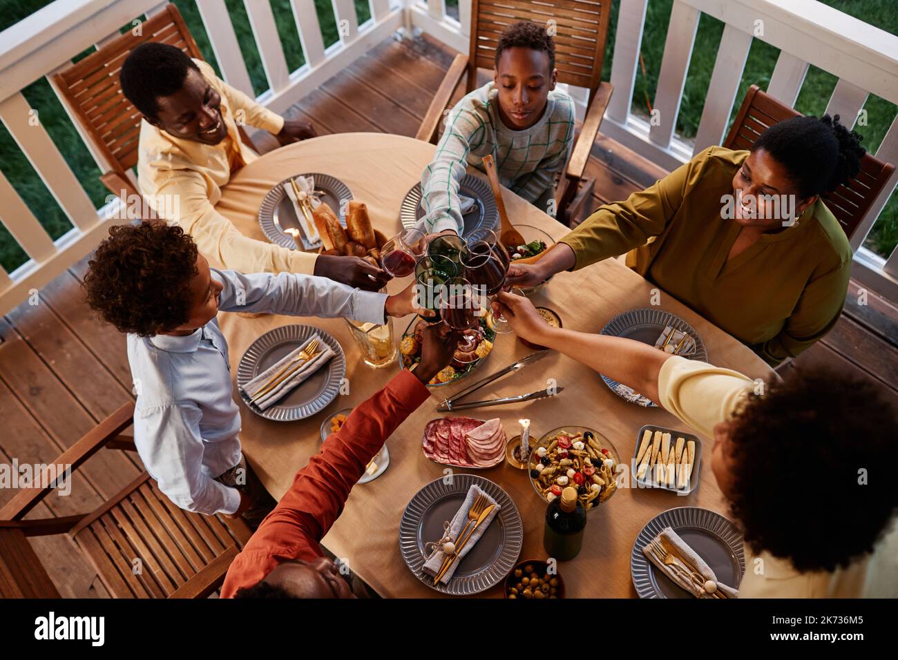 Blick aus dem hohen Winkel auf große afroamerikanische Familie klirrende Gläser über dem Esstisch im Freien in gemütlicher Abendumgebung Stockfoto
