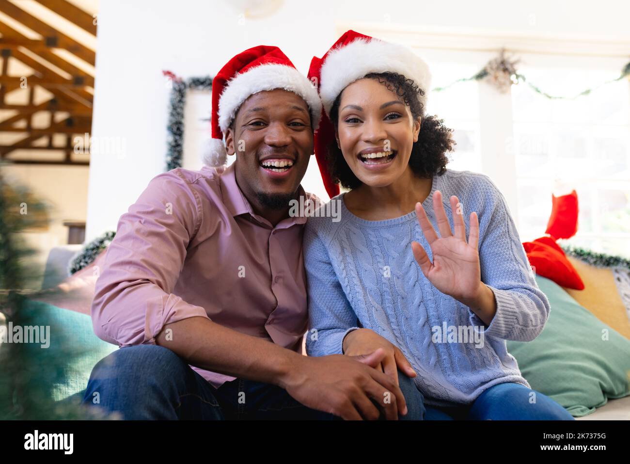Glückliches afroamerikanisches Paar, das das Haus des weihnachtsmanns trägt und ein Videogespräch hat Stockfoto