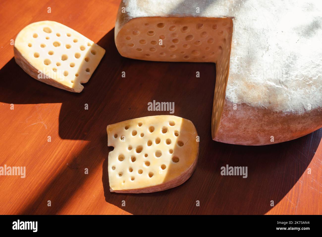 Nahaufnahme eines Rades und geschnittener Gruyere-Käse auf Holzboden. Natürliches Gourmet-Konzept. Hochwertige Fotos Stockfoto