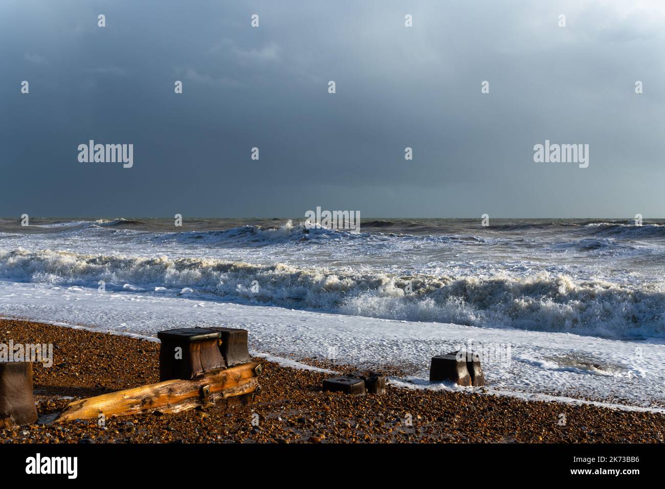 Wellen brechen am Strand von Bexhill-on-Sea mit Sturmwolken und einem Strand groyne Stockfoto