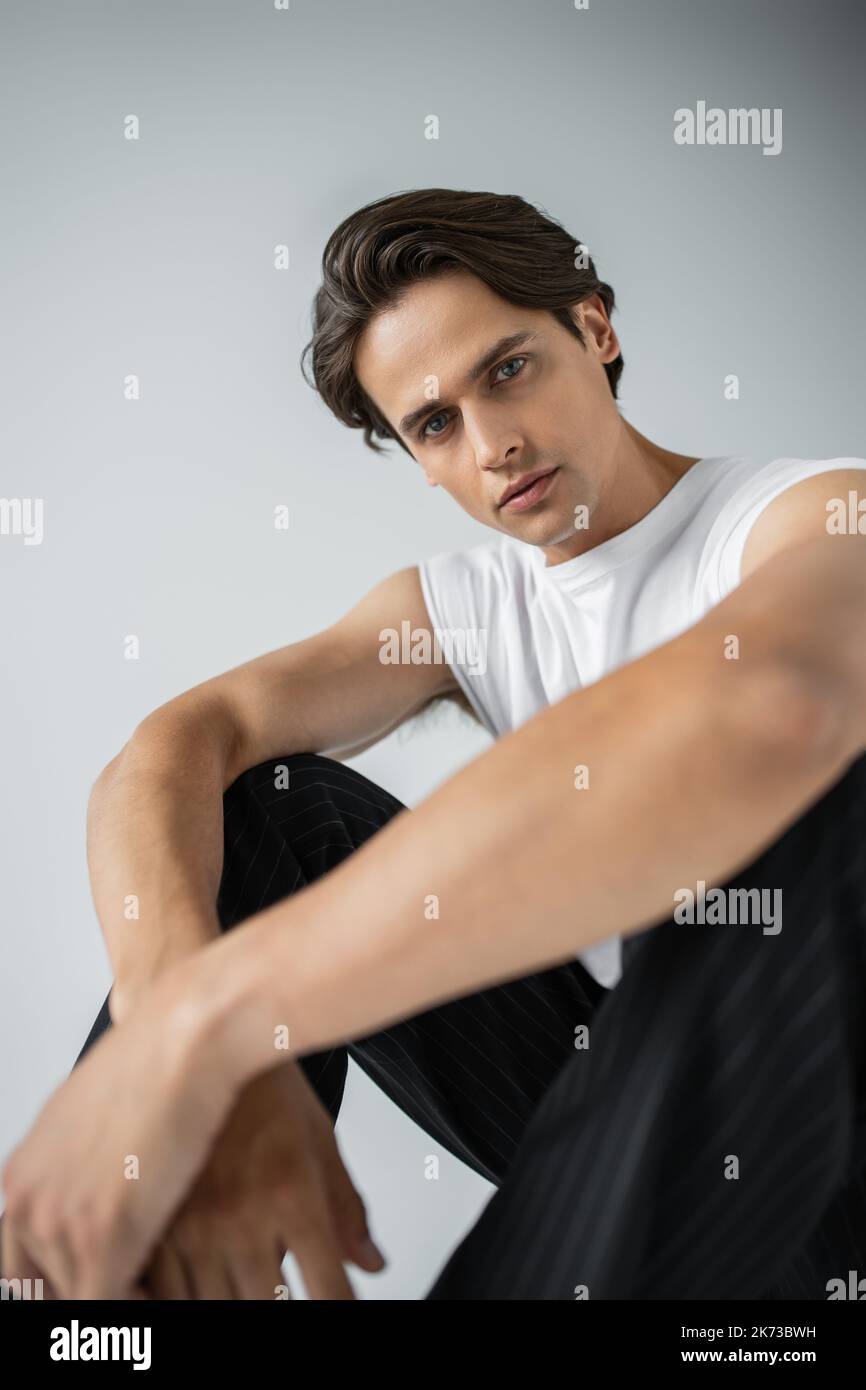 Gut aussehender Mann in gestreifter Hose und weißem T-Shirt auf grauem Sitz Stockfoto