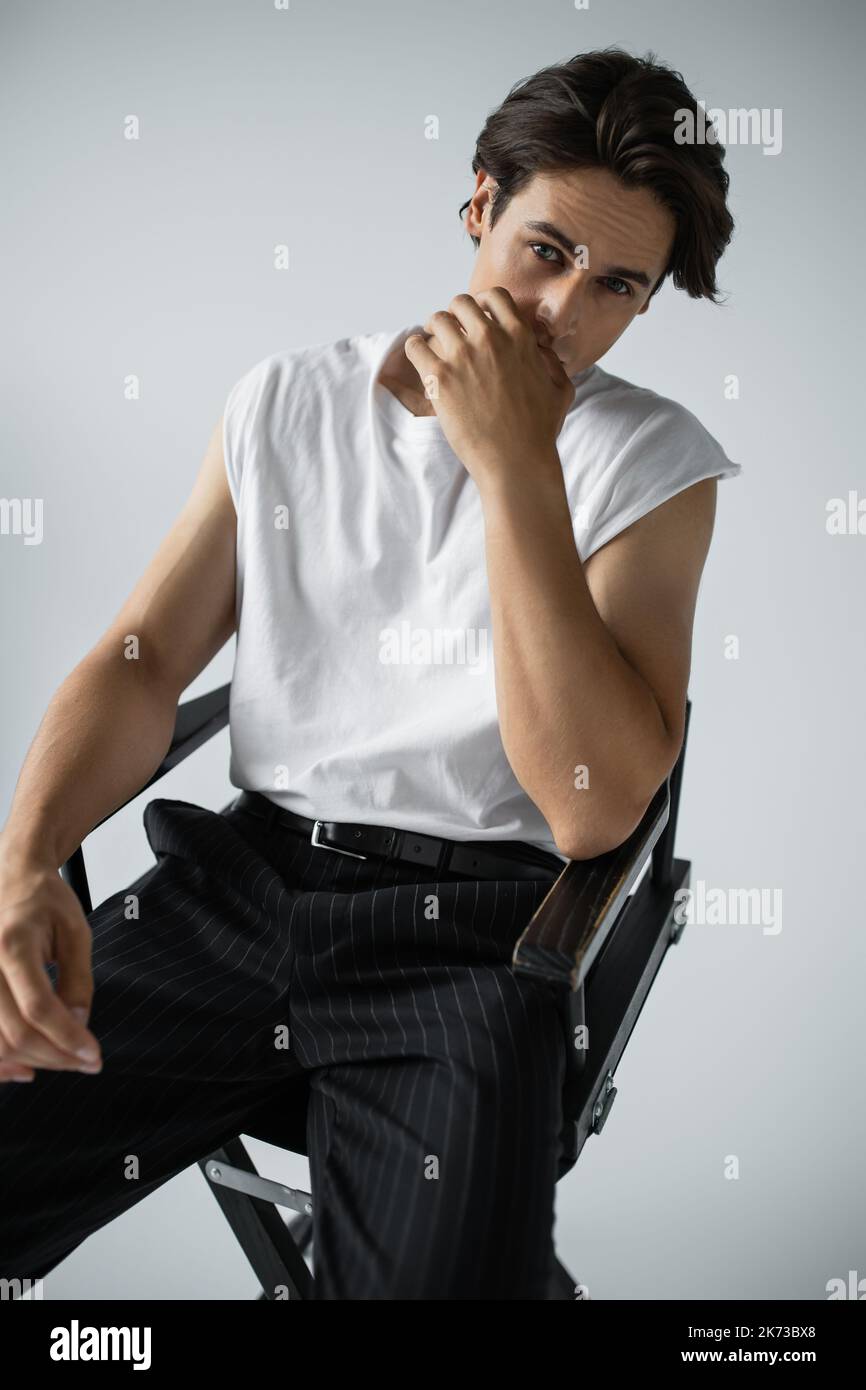 Brünett Mann in gestreiften Hosen und weißen T-Shirt sitzt auf Lagerstuhl auf grau Stockfoto