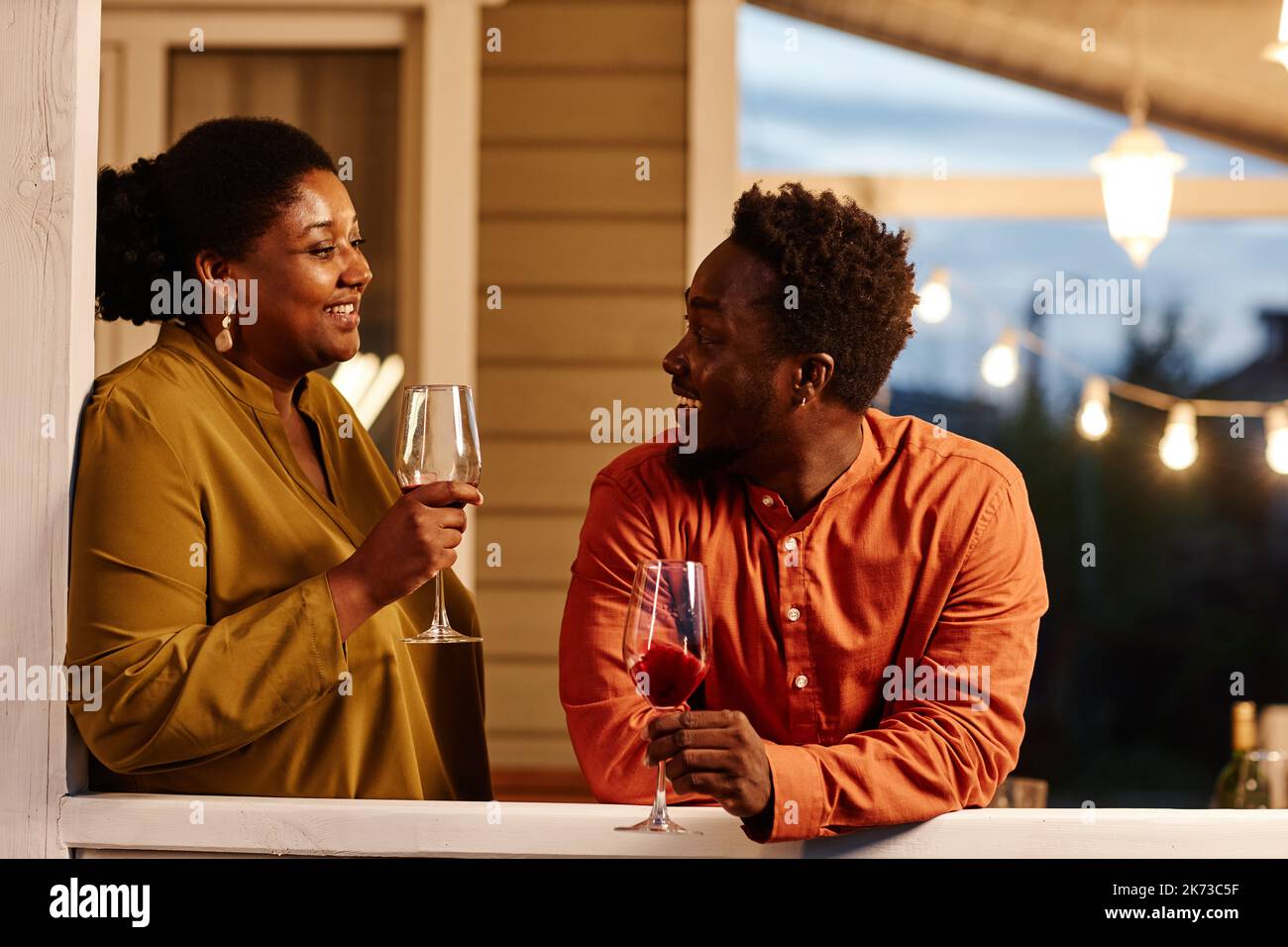 Porträt eines jungen afroamerikanischen Paares, das abends auf der Terrasse des Hauses Wein genießt Stockfoto