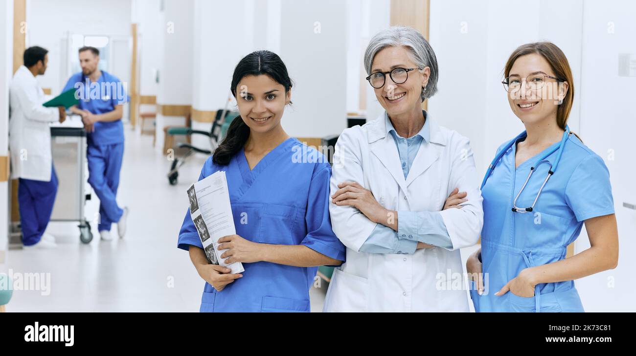 Multinationales medizinisches Team. Porträt eines reifen Chefarztes mit zwei Krankenschwestern, die auf dem Flur des Krankenhauses stehen und die Kamera betrachten Stockfoto