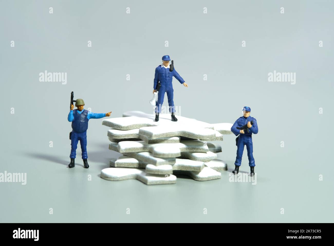 Miniatur Menschen Spielzeug Figur Fotografie. Konzept der Schutzstrategie. Ein Sicherheitsbeamter, der über einem weißen Puzzleteil steht. Isoliert auf grauem Rücken Stockfoto