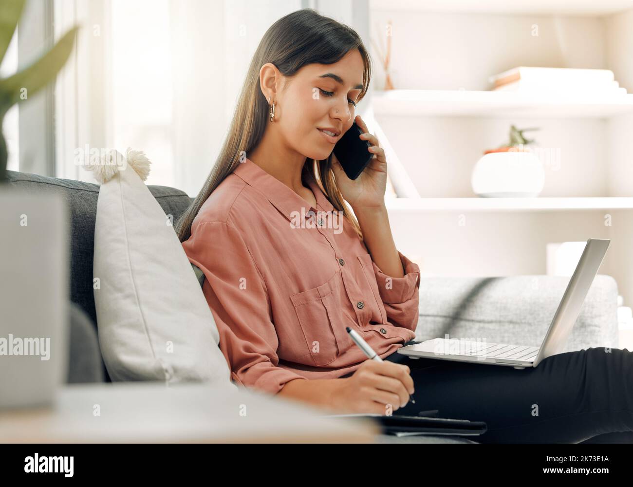 Arbeiten von zu Hause aus für den Tag. Eine junge Frau, die zu Hause ein Telefon und einen Laptop benutzt. Stockfoto
