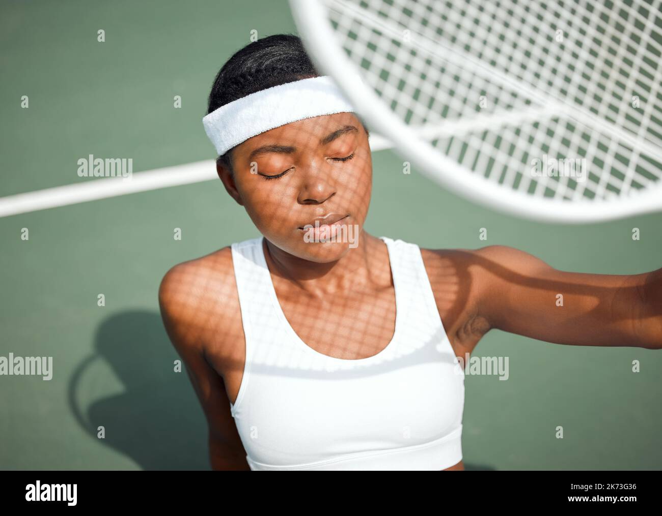 Sie leuchtet anders. Eine sportliche junge Frau, die ihr Gesicht mit einem Tennisschläger auf einem Platz vor der Sonne schützt. Stockfoto