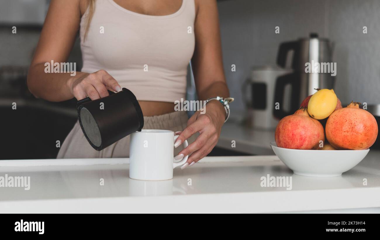 Weißer Becher-Mockup. Weiße Tasse Mockup für Tasse Verkäufer und Designer. Eine schöne und hübsche Frau in einer modernen Küche gießt Kaffee in eine weiße leere Tasse Stockfoto