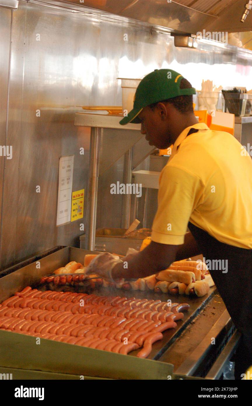 Ein junger Mann kocht dutzende Hot Dogs und Frankfurter in Nathans in Coney Island, Brooklyn, New York, dem Gründungsort der Fast-Food-Restaurants Stockfoto