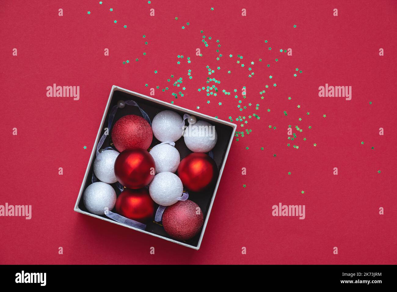 Draufsicht auf runde Weihnachtsdekorationen in offener Geschenkbox auf rotem Hintergrund. Schöne rote und weiße runde Spielzeuge. Konzept von Weihnachten und Neujahr. Speicherplatz kopieren. Weicher, selektiver Fokus Stockfoto