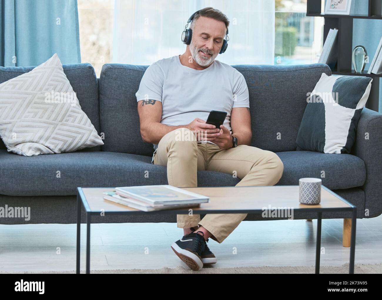 Das Traumleben leben leben. Ein reifer Mann, der zu Hause mit seinem Smartphone Musik hört. Stockfoto