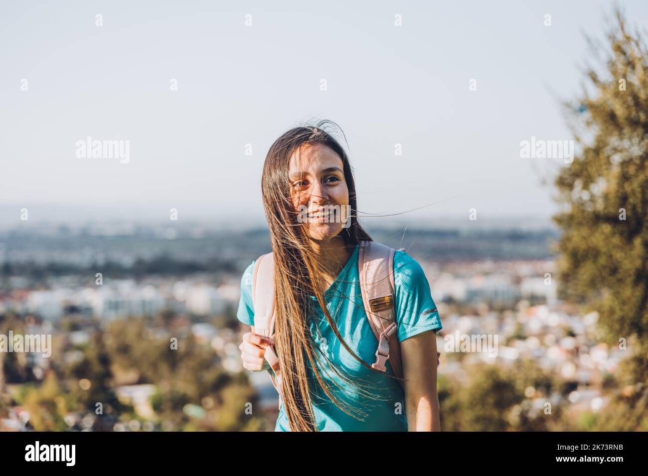 Lächelnde junge Frau mit einem Rucksack auf der Spitze eines Hügels. Selbstvertrauen. Stockfoto