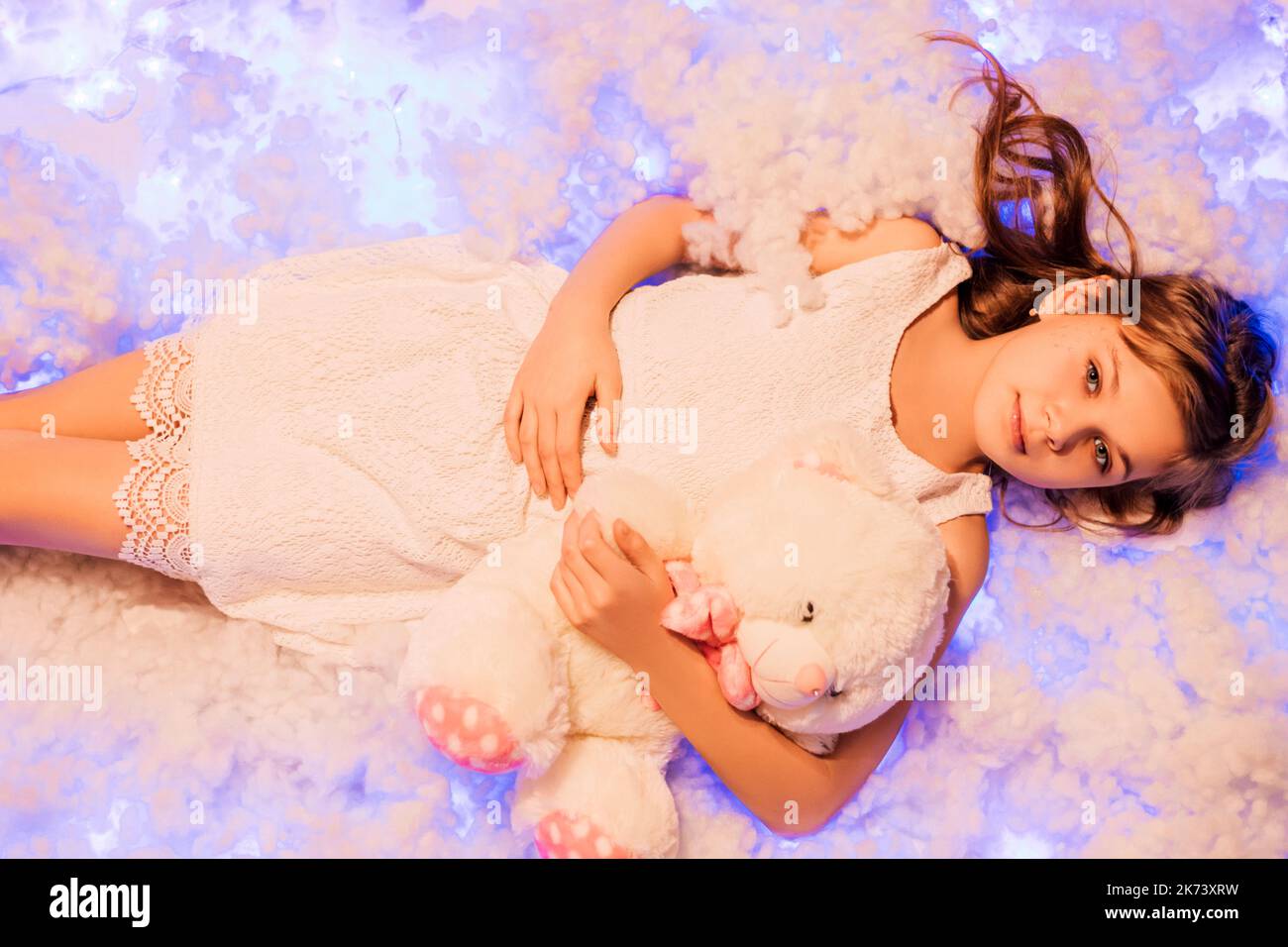 Ein Mädchen mit Teddybären in einem leichten Kleid liegt in den Wolken Stockfoto