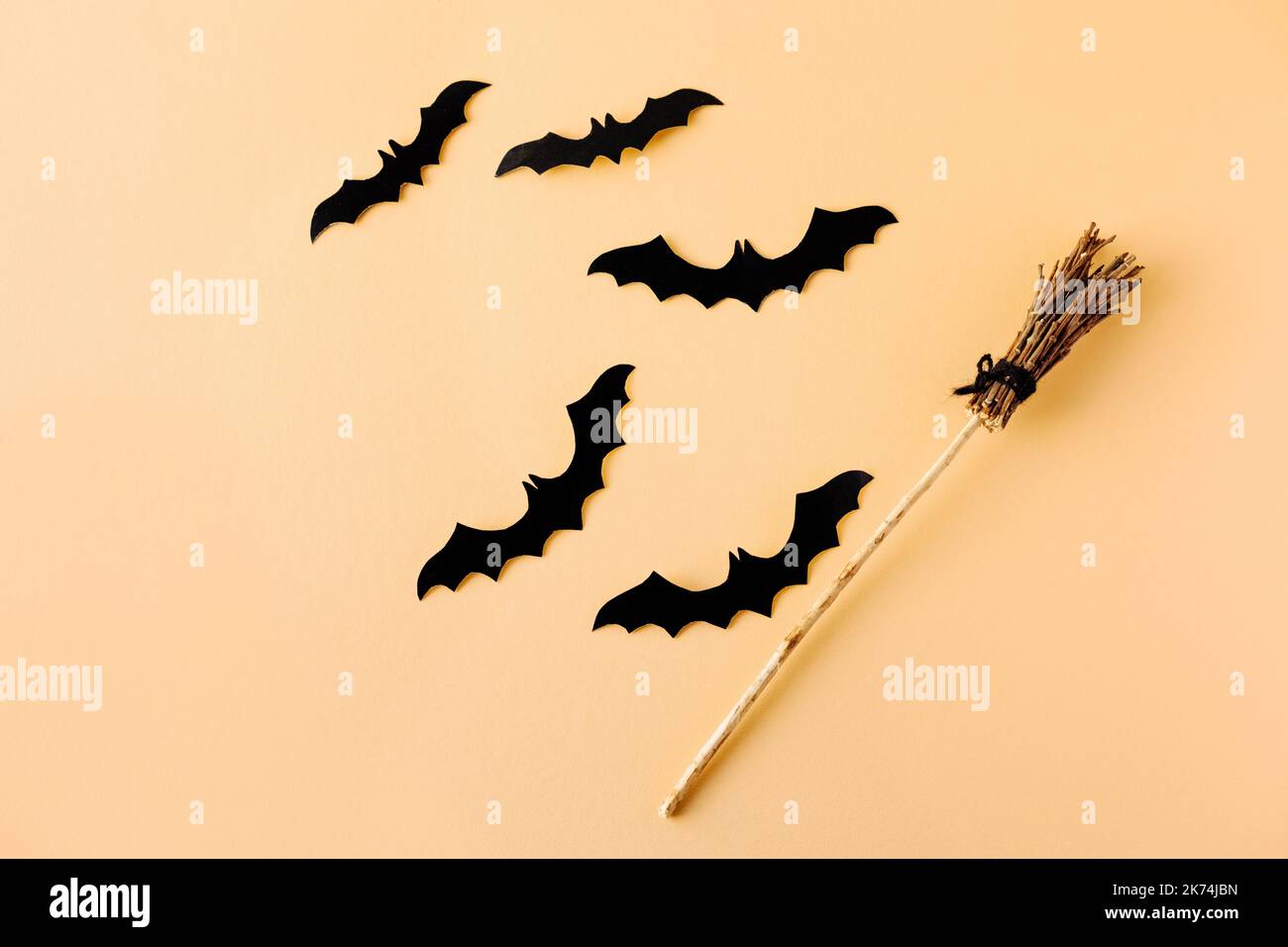 Halloween-Konzept. Ein Hexenbesen und schwarze Fledermäuse auf orangefarbenem Hintergrund Stockfoto