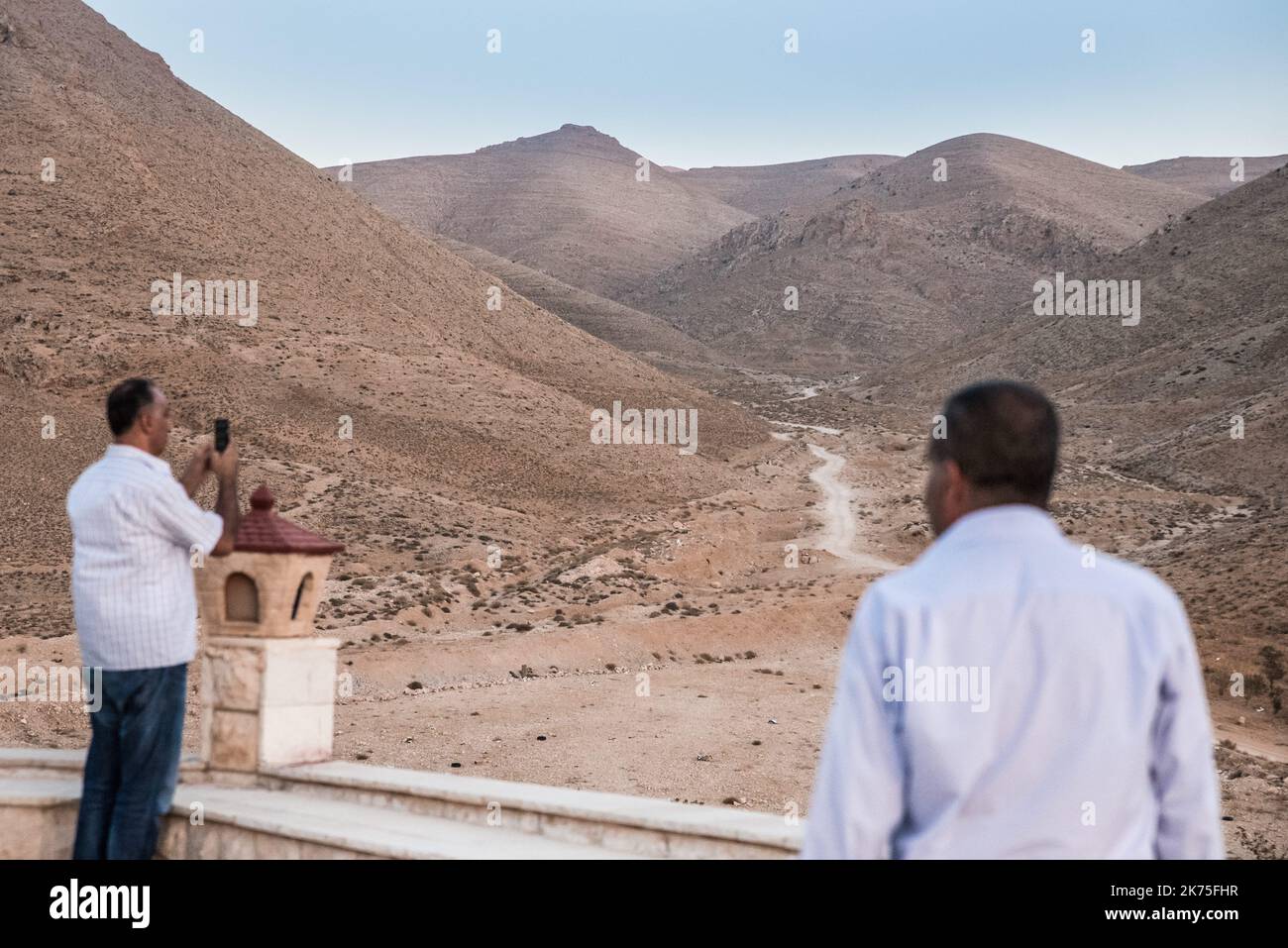 15/08/2017 - Libanon / Qaa - Männer schauen sich die Berge an, in denen sich Daesh einige Kilometer weiter befindet, während der Assomptionszeremonie. Zurück in das Dorf Al-Qaa, eine christliche Hochburg im Libanon an der syrischen Grenze, ein Jahr nach der Anschlagswelle von Daesh. Im Juni 2017 starten die libanesische Armee und die Hisbollah eine Offensive, um die Positionen der islamistischen Gruppe in den Bergen auszurotten. Als Zeichen des Widerstands feiern die Bewohner ihre erste religiöse Zeremonie an den Uschwellen des Dorfes, in der Nähe von Daesh's Positionen. Stockfoto