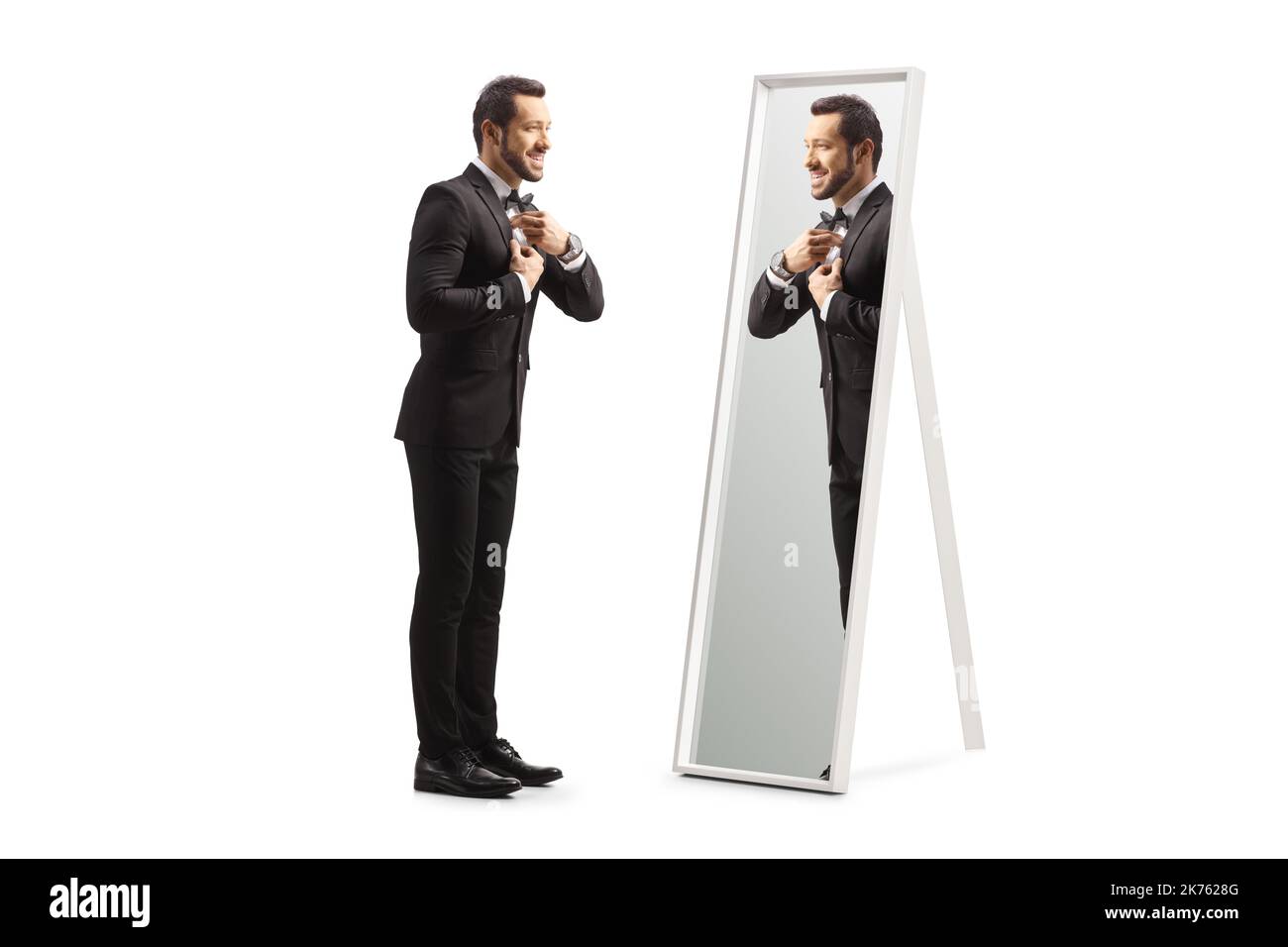 In voller Länge Profilaufnahme eines jungen eleganten Mannes, der sich vor einem auf weißem Hintergrund isolierten Spiegel fertig gemacht hat Stockfoto