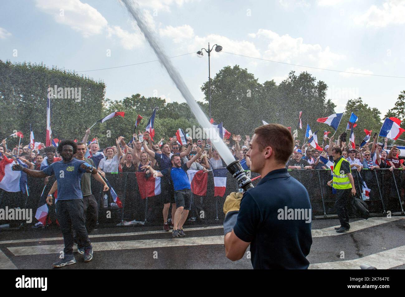 UN pompier avec une lance a incendie arrose les Supporters français dans la Fan Zone du CHAMP de Mars lors De la finale de la Coupe du monde de Football 2018 Ein Feuerwehrmann mit Feuerwehrschlauch sprüht französische Fans In die Fan-Zone des „CHAMP de Mars“ während des Finales der FIFA-Weltmeisterschaft 2018 am 15 2018. Juli.NUR FRANKREICH Stockfoto