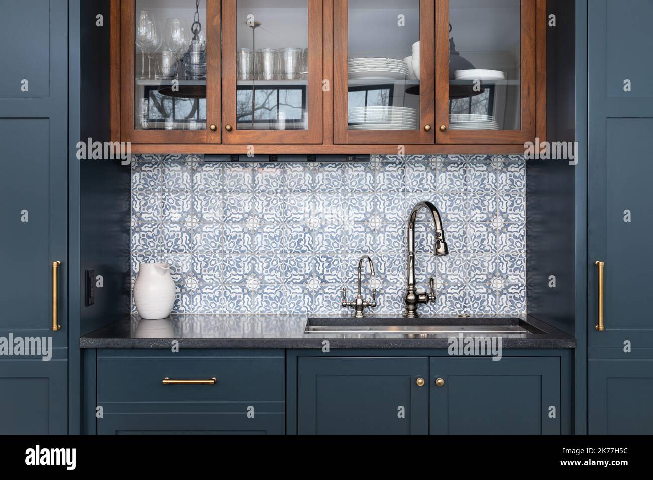 Ein Küchenwaschbecken mit einem schönen Muster gekachelten Backsplash mit einem Chrom-Wasserhahn, schwarzen Granit-Arbeitsplatten, und umgeben von blauen und Holzschränken. Stockfoto
