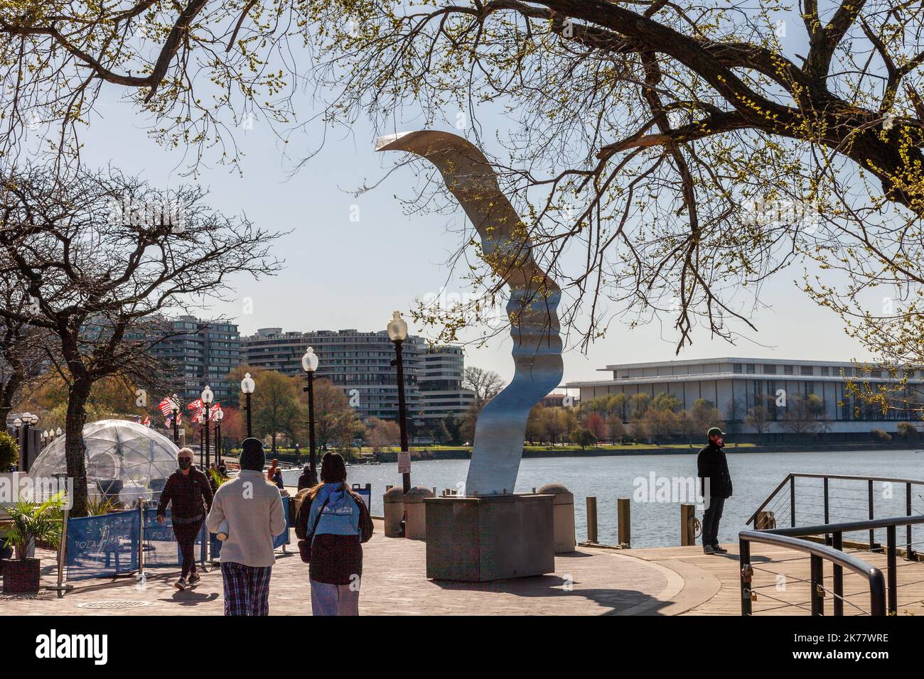 Ein Blick auf ein Denkmal und Menschen, die mit dem Potomac-Fluss in Washington und dem Kennedy Center und Watergate Complex Gebäude im Hintergrund spazieren gehen. Stockfoto