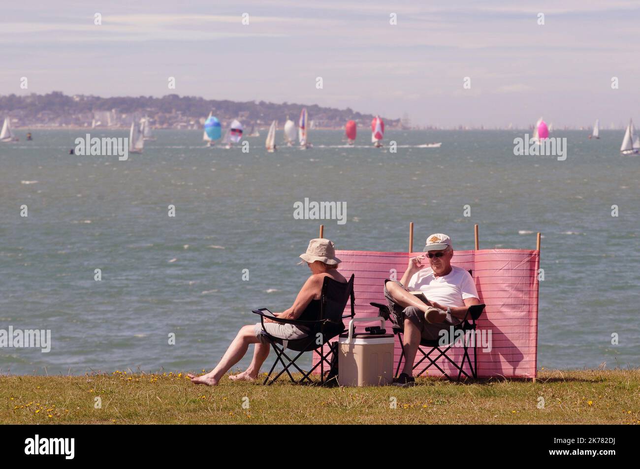 Ein Paar genießt die Sonne im Lee on the Solent, Hampshire, während die Teilnehmer der Cowes Week im Solent hinter ihnen gegeneinander antreten. Pic Mike Walker, 2015 Stockfoto