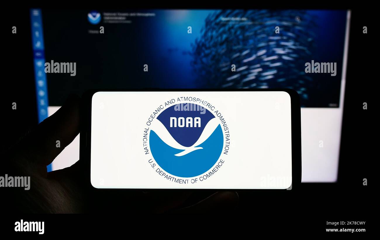 Person mit Telefon und Logo der National Oceanic and Atmospheric Administration (NOAA) auf dem Bildschirm vor der Website. Konzentrieren Sie sich auf die Telefonanzeige. Stockfoto