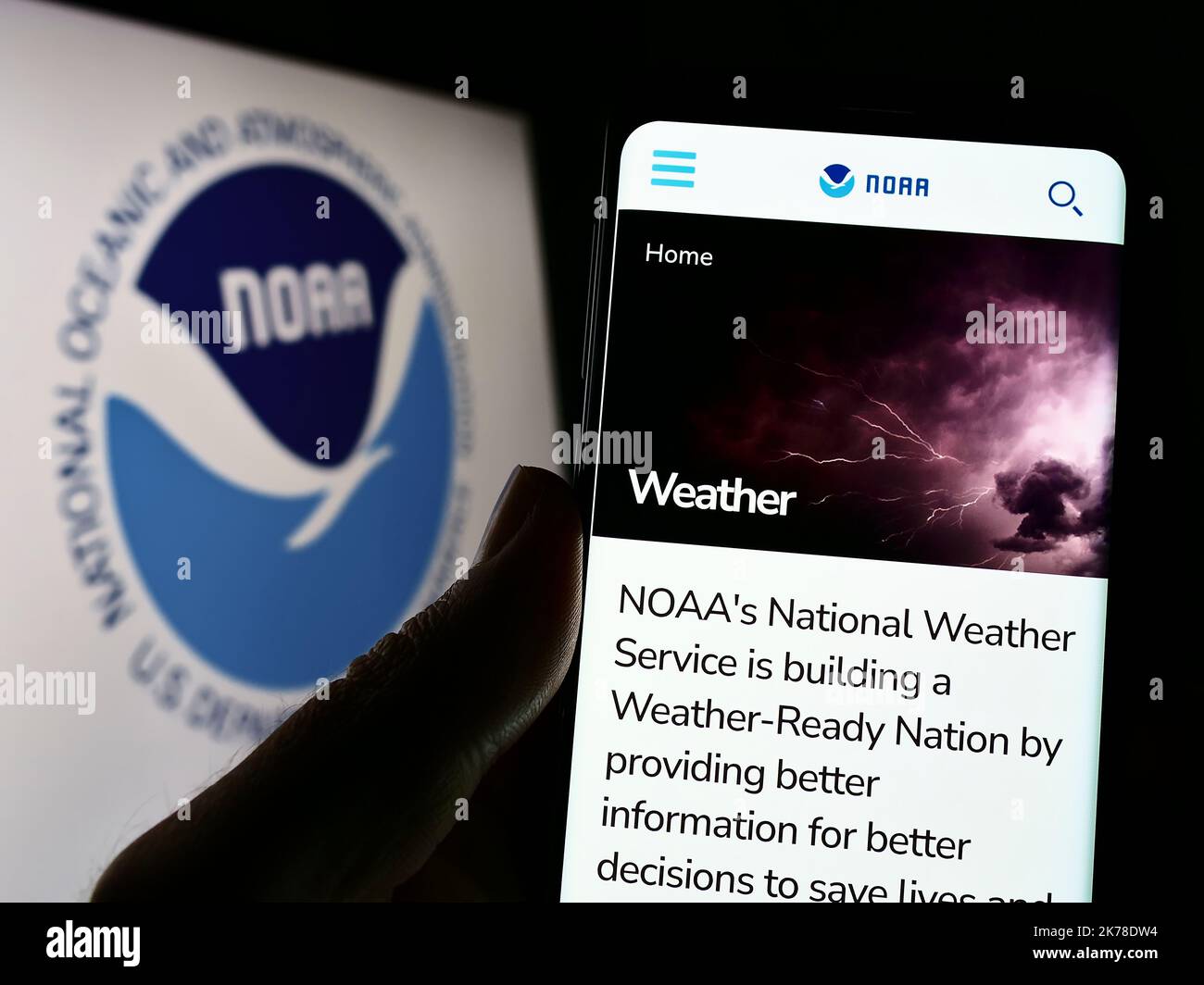 Person mit Telefon und Webseite der National Oceanic and Atmospheric Administration (NOAA) auf dem Bildschirm mit Logo. Konzentrieren Sie sich auf die Mitte des Telefondisplays. Stockfoto