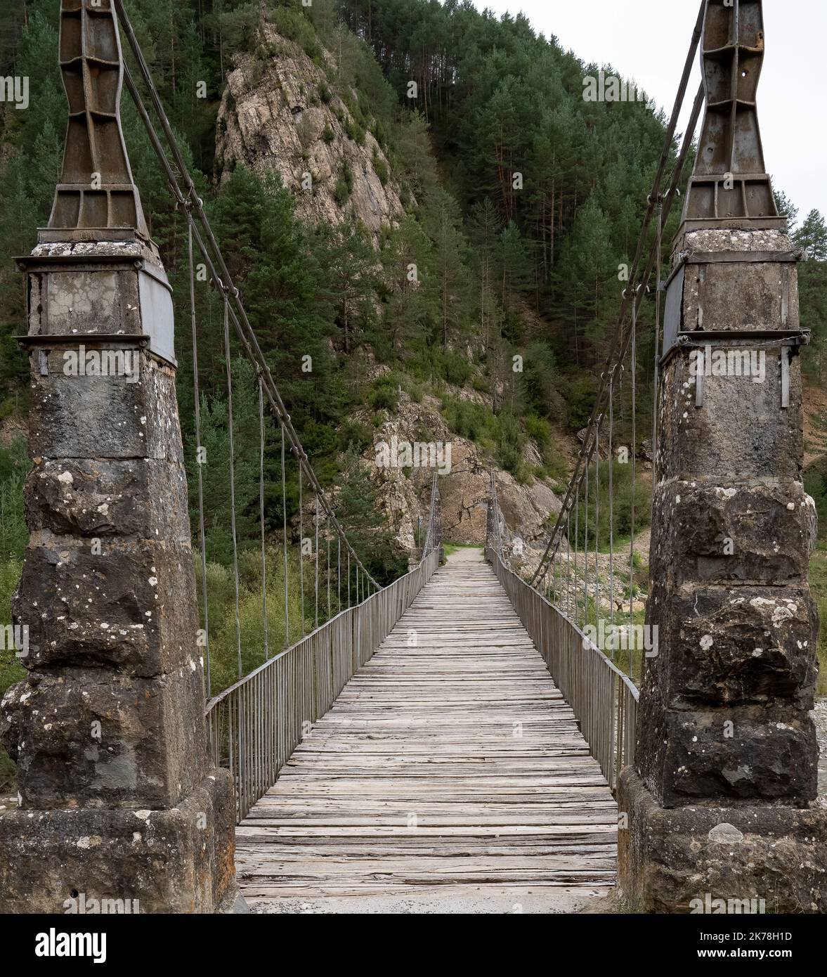 Ein steinerner Pier, eine Hängebrücke mit Kabelaufhängung über einen Bergfluss Stockfoto