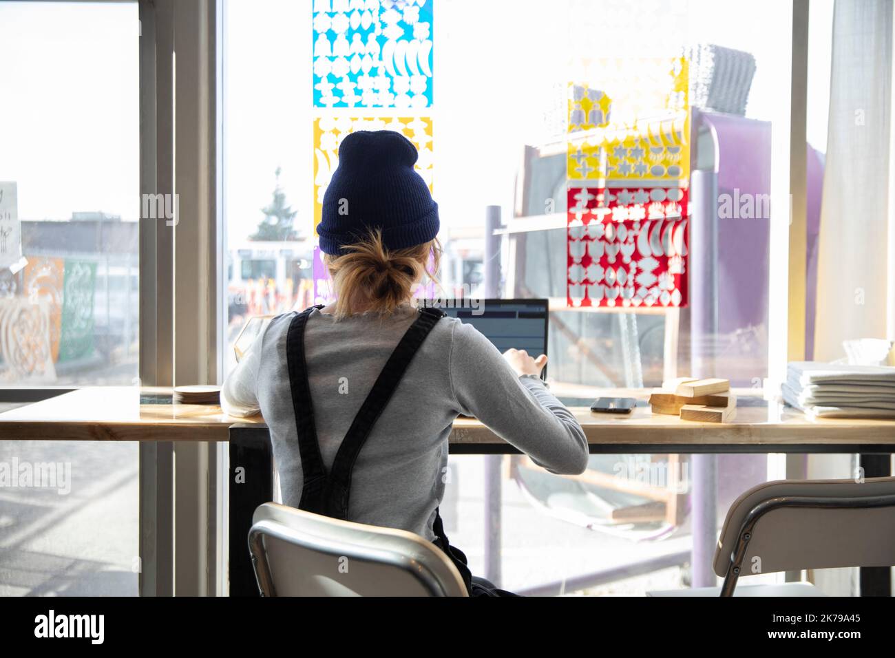 Eine Studentin mit Hut, die einen Laptop am Fenster trägt Stockfoto