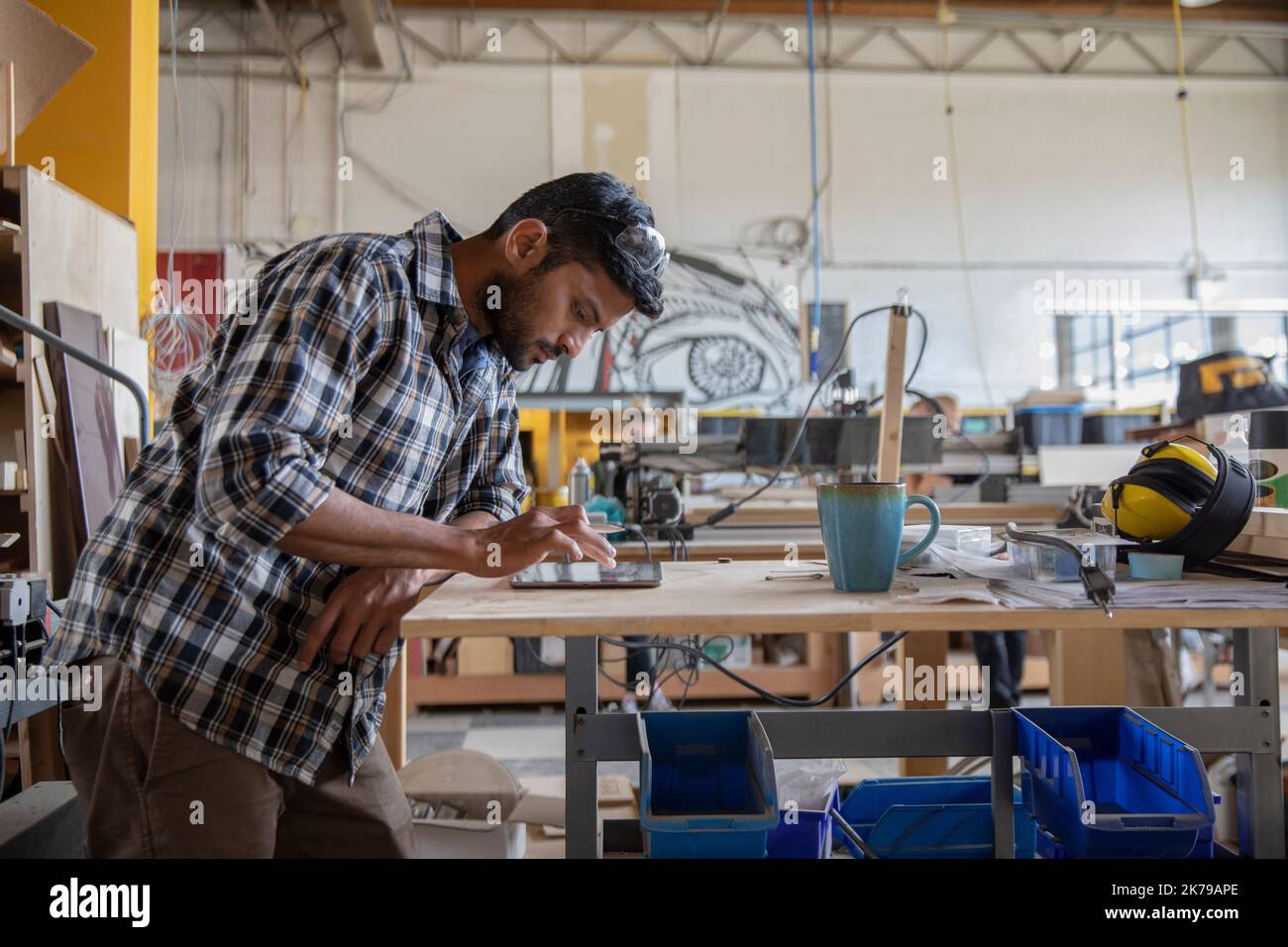 Junger Mann, der ein digitales Tablet auf einer Werkbank im Maker-Bereich benutzt Stockfoto