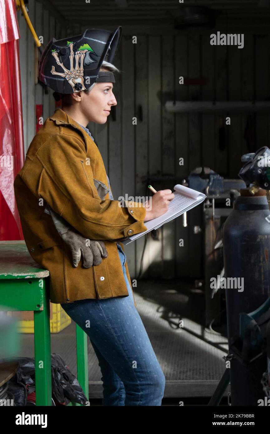 Junge Frau in der Werkstatt, die Schutzhelm trägt und Notizen macht Stockfoto