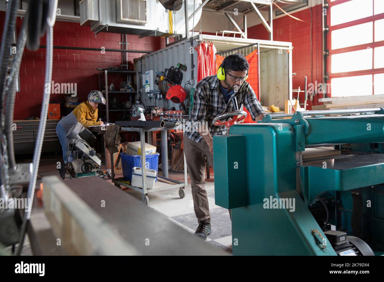 Junger Mann mit Kapselgehörschutz, der eine Maschine im Makerraum benutzt Stockfoto