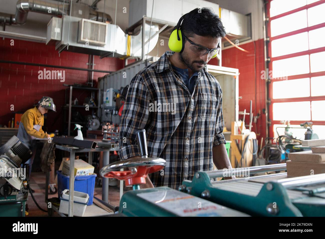 Junger Mann mit Kapselgehörschutz, der eine Maschine im Makerraum benutzt Stockfoto