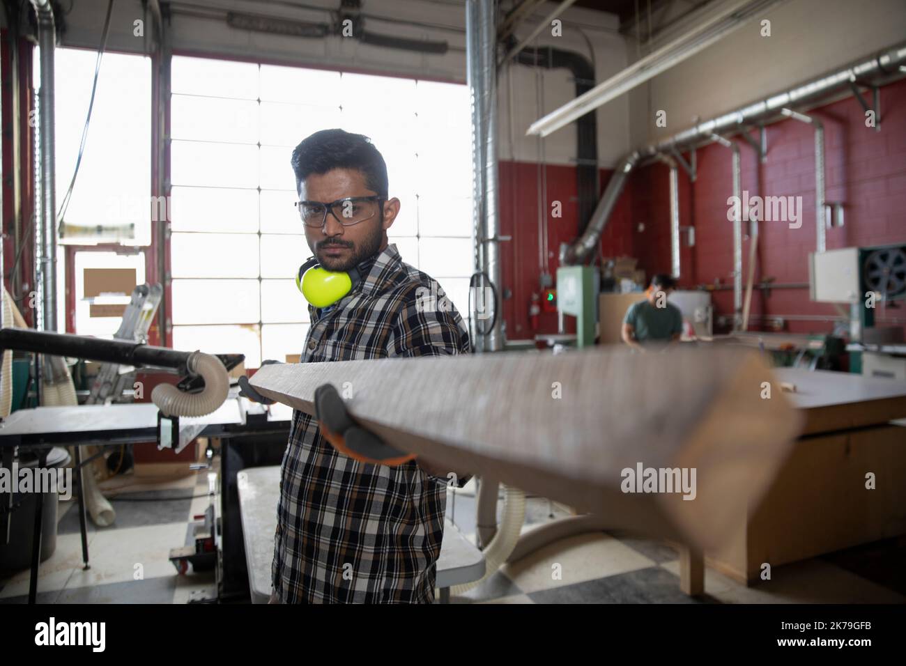Mann trägt schützende Arbeitskleidung und hält Holz im Makerbereich Stockfoto