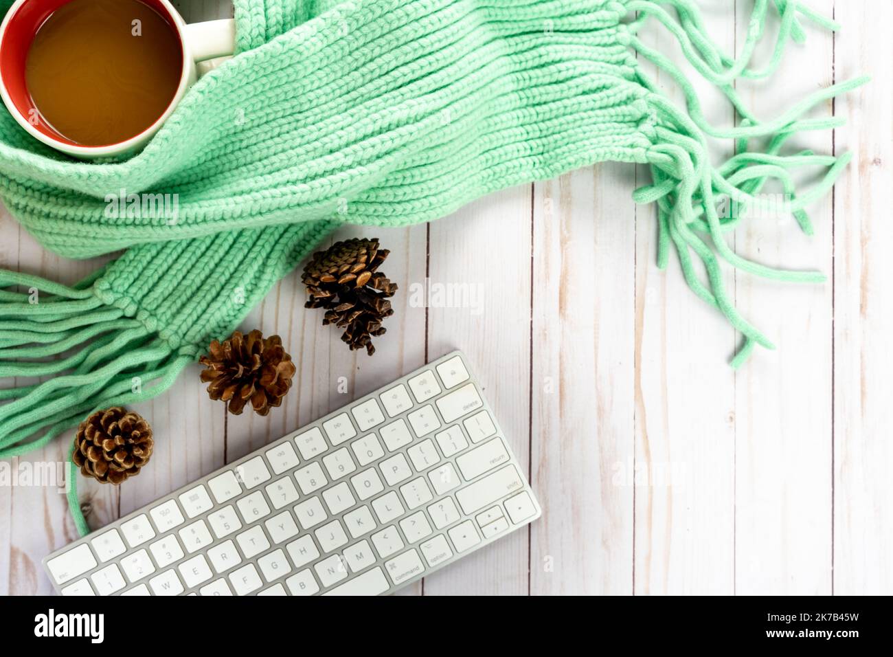 Blogger Fall gemütlicher Pullover Wetter Herbst Arrangement, mit weißer Tastatur, Pinienzapfen, Zopfmuster blauem Schal und Kaffeebecher auf Holz Hintergrund Stockfoto