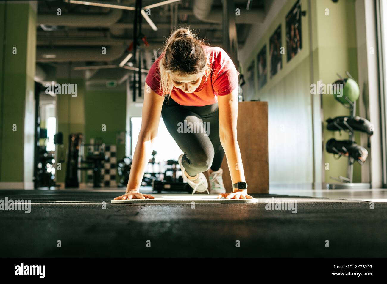 Plus Size Mädchen stehen auf ausgestreckten Armen und abwechselnd Flex Beine Blick nach unten in Fitness-Studio. Junge Frau macht Stretching-Training auf der Matte. Schulung in Stockfoto