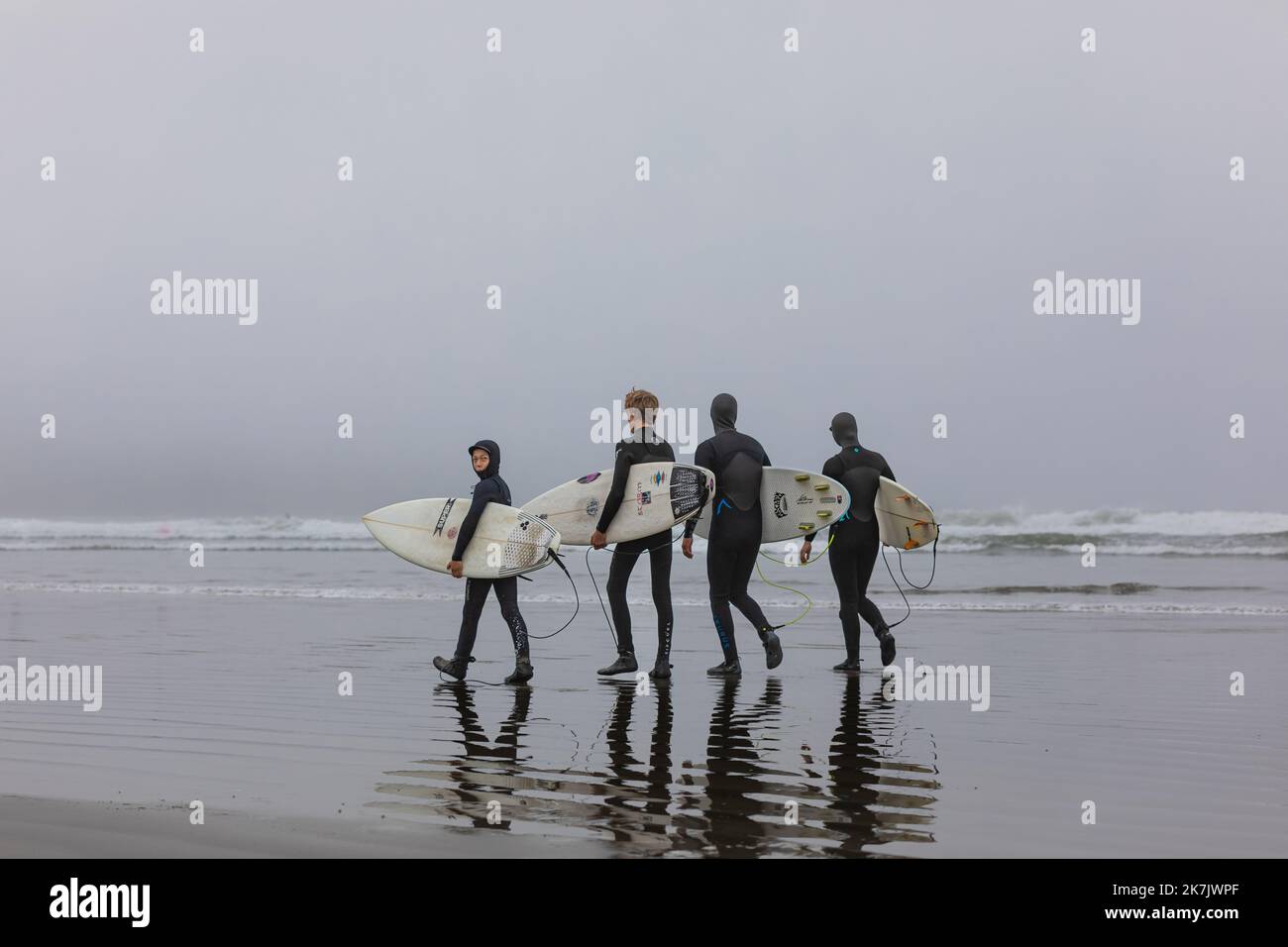 Gruppe von Surfern, die ihre Surfbretter bei nebligen Sonnenaufgängen tragen. Surfer in Neoprenanzügen am Strand in Tofino Kanada. Reisefoto, selektiver Fokus, Copyspa Stockfoto