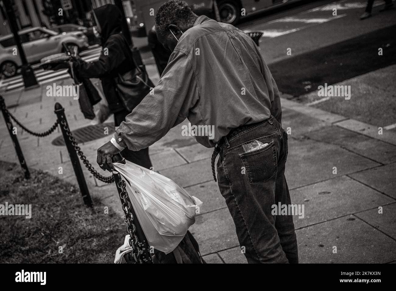 Ein Mann ruht auf einem Kettengliederposten, während Freiwillige von Marthas Table am Donnerstag, 13. Oktober 2022, am McPherson Square in Washington, DC, warme Mahlzeiten und andere Lebensmittel an Obdachlose verteilen. Es gibt etwa drei Dutzend Zelte im Park, mit Waschküche, die an Ästen, Stühlen, Tischen und sogar zwei tragbaren Badezimmern hängt. Kredit: Rod Lampey/CNP (BESCHRÄNKUNG: KEINE New York oder New Jersey Zeitungen oder Zeitungen innerhalb eines 75 Meilen Radius von New York City) Stockfoto