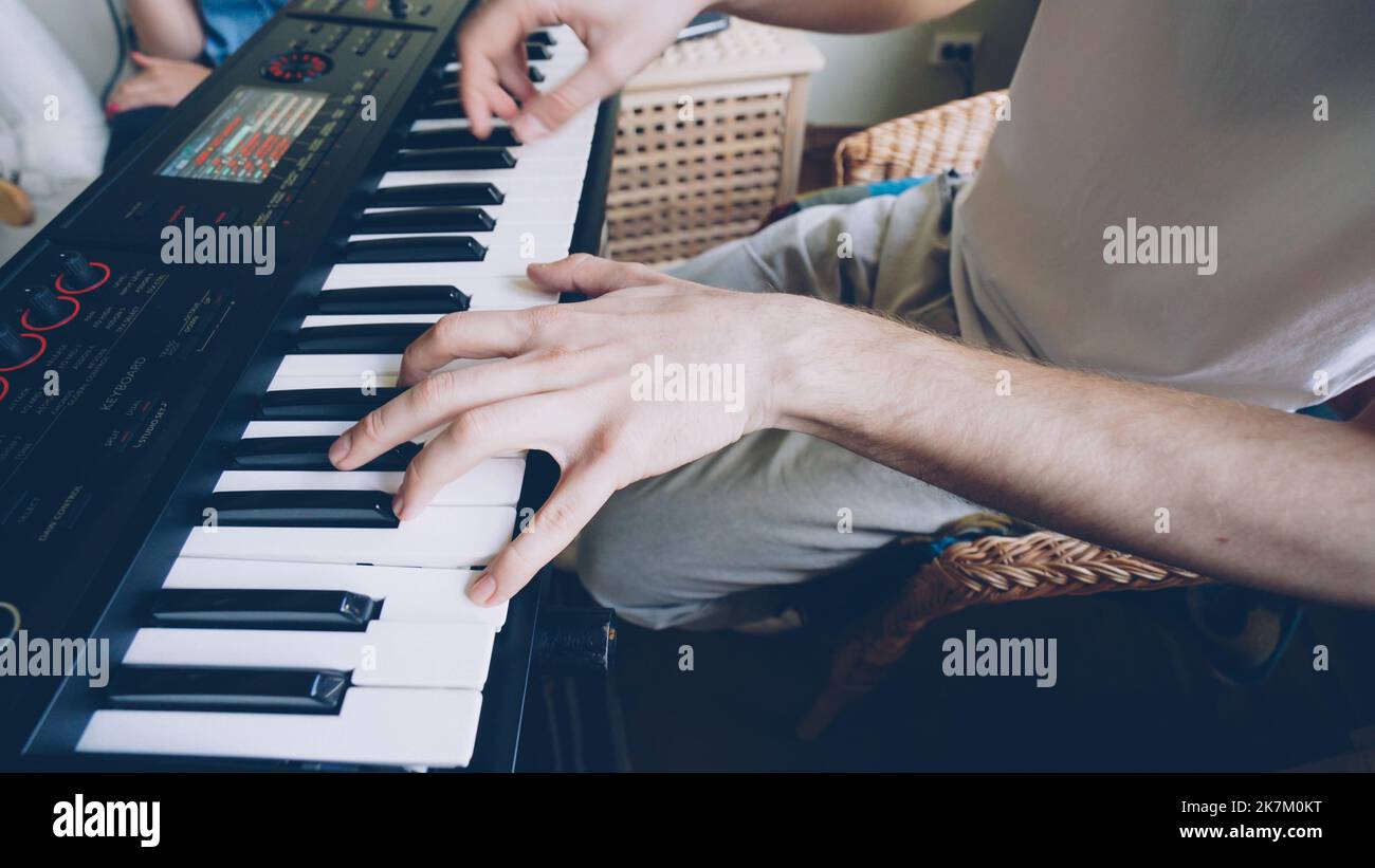 Der junge bärtige Keyboarder spielt Keyboard, während seine Freunde zu Hause bei der Probe spielen. Nahaufnahme der Hände auf den Tasten. Stockfoto