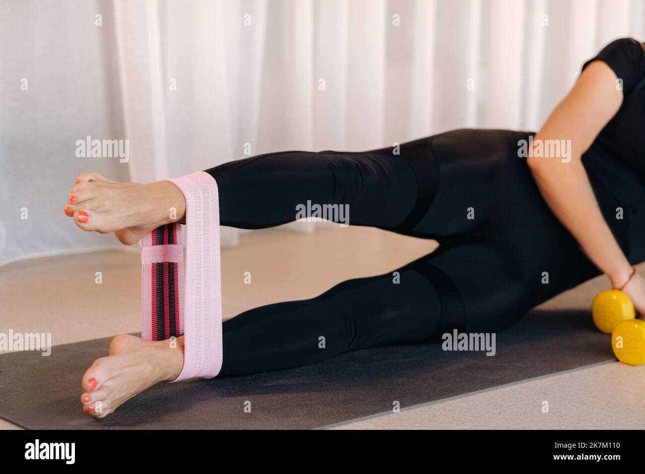 Eine Frau in einem Fitnessraum führt Crossfit-Übungen mit einem rosa elastischen Expander durch, der ihre Beine im Fitnessstudio dehnt Stockfoto