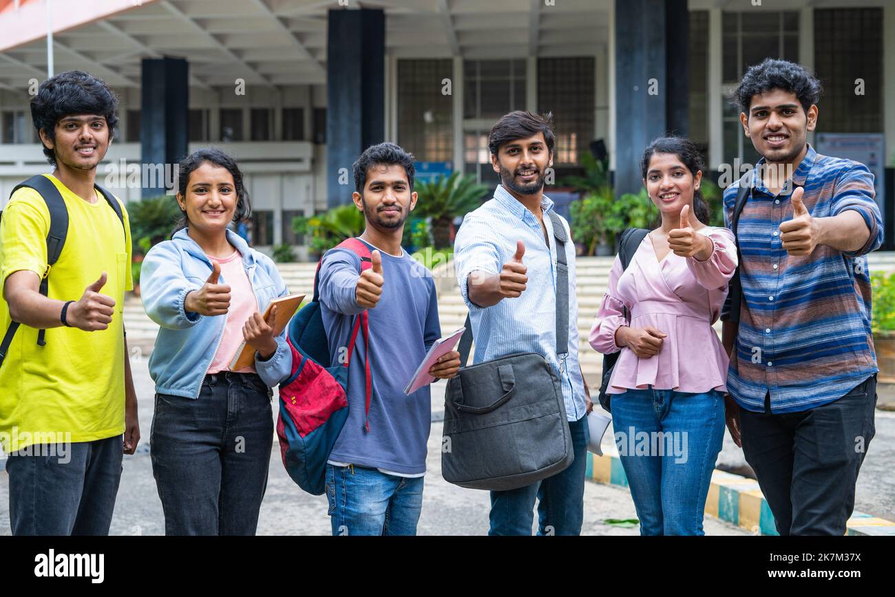 Selbstbewusste Studenten mit Rucksack und Büchern, die durch die Kamera auf dem College-Campus Daumen nach oben zeigen - Konzept der Genehmigung, Bildung und Entwicklung. Stockfoto