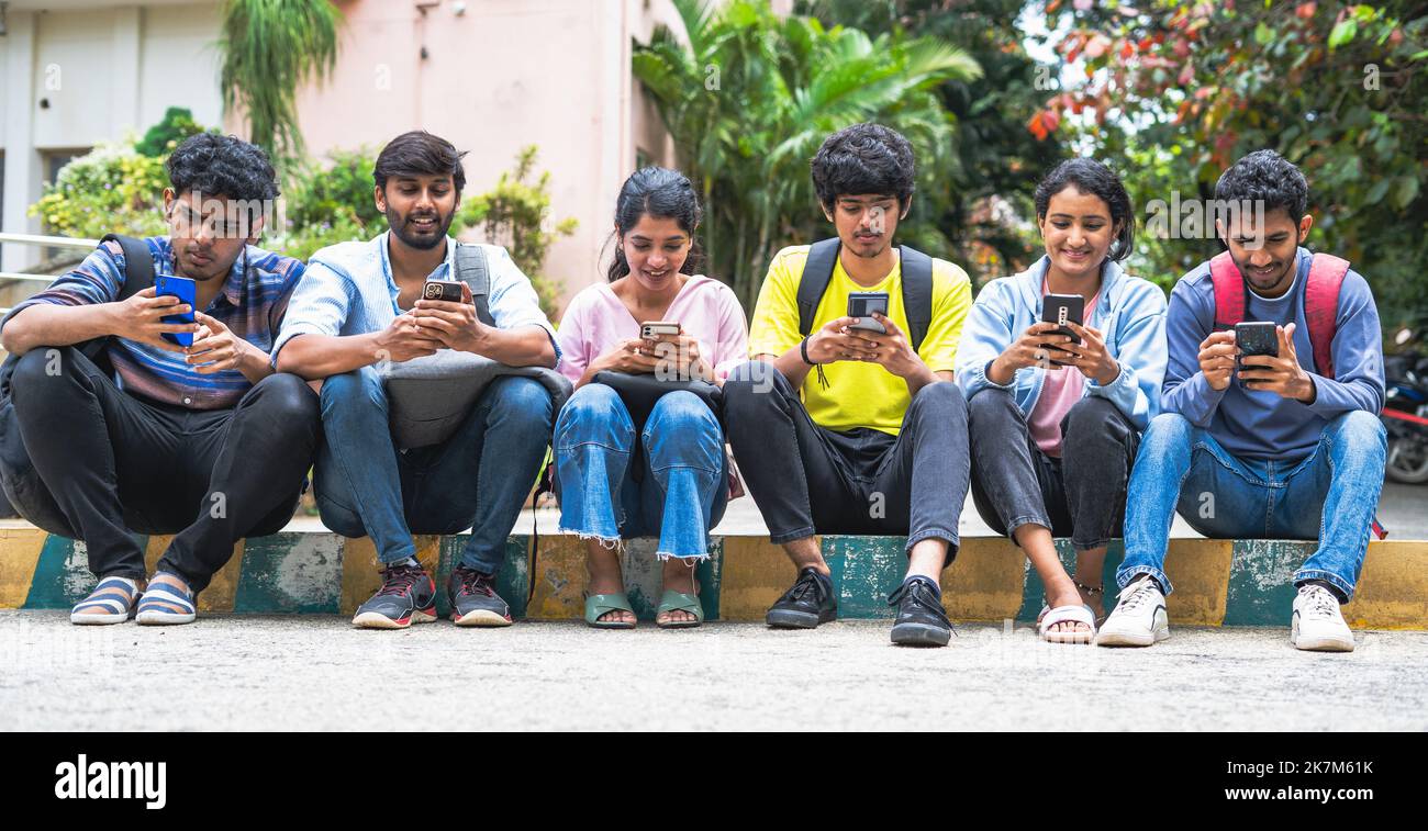 Eine Gruppe indischer College-Studenten, die in der Freizeit mit dem Mobiltelefon auf dem Campus beschäftigt sind – Konzept des Social Media Sharing, der Bildung und des Internets. Stockfoto