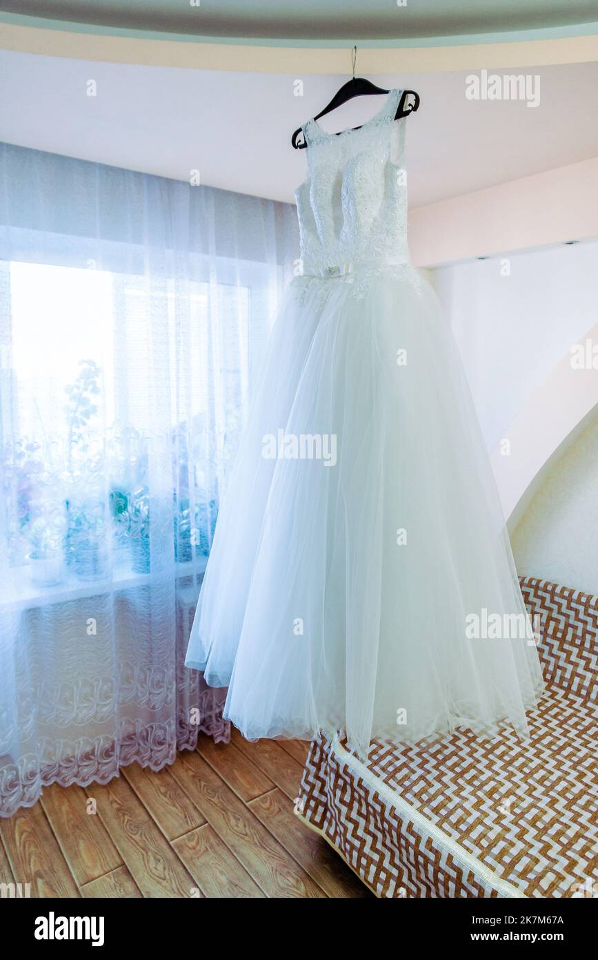 Das perfekte Hochzeitskleid mit einem vollen Rock auf einem Kleiderbügel in das Zimmer der Braut mit blauen Vorhängen Stockfoto