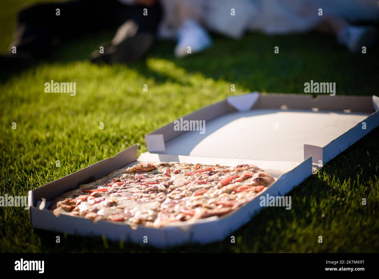 Ein fröhliches Paar junger Leute, die Spaß haben, auf dem Boden zu sitzen, Wein zu trinken und Pizza zu beißen - ein Lifestyle-Konzept für romantische Leute Stockfoto