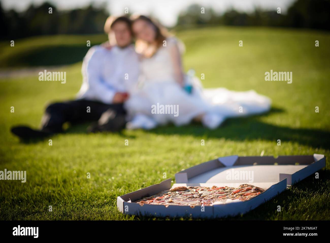 Ein fröhliches Paar junger Leute, die Spaß haben, auf dem Boden zu sitzen, Wein zu trinken und Pizza zu beißen - ein Lifestyle-Konzept für romantische Leute Stockfoto