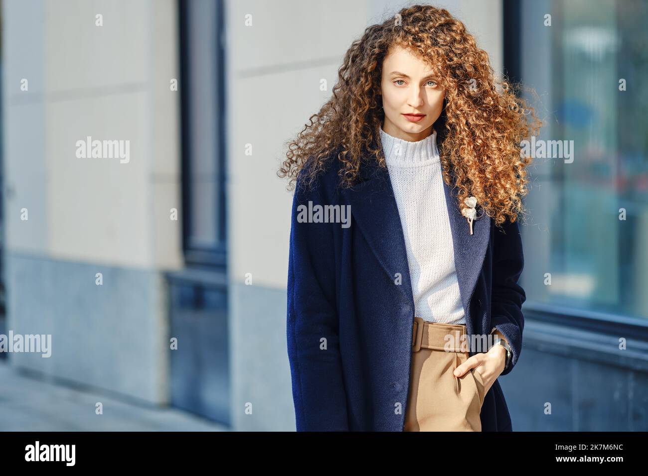 Junge ehrgeizige Frau im Wollmantel, die auf der Straße geht Stockfoto